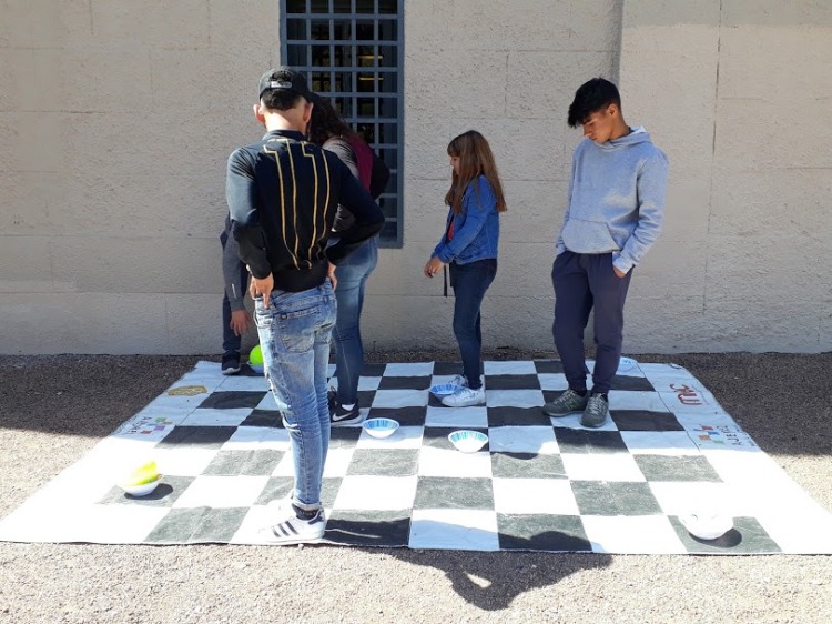 tablero grande de ajedrez, jovenes parados sobre él
